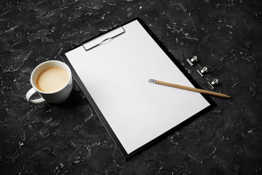 Blank clipboard, coffee cup and pencil on black plaster background. Copy space for text.