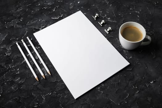 Photo of blank stationery set on black plaster background. Clipboard, letterhead, coffee cup and pencils.