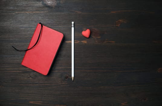 Photo of blank red notebook, pencil and heart-shaped eraser on wood table background. Branding mock up. Space for text. Flat lay.