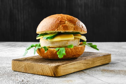 Homemade fishburger with cheese, arugula and cucumber on wooden cutting board