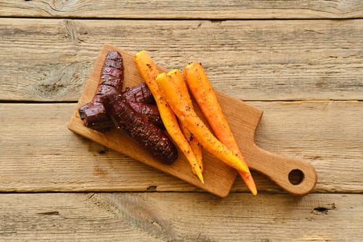Overhead view of baked carrot and beetroot with salt and pepper on wooden board
