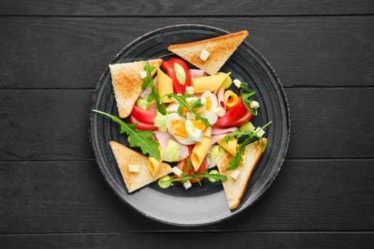 Overhead view of boiled eggs with slices of toast, cheddar, ham and tomato on black wooden table
