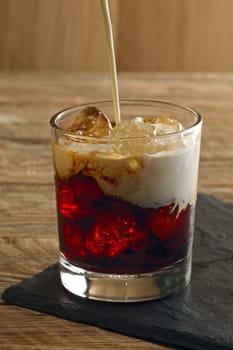 Pouring cream into cocktail White Russian. Vodka, coffee liquor, cream and ice