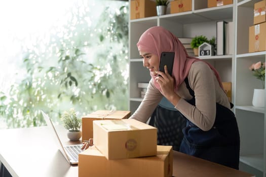 A Muslim woman is engaged in her online business, packing and preparing shipments in a bright and organized workspace.