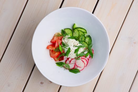 Top view of salad with radish, tomato, cucumber, onion and sour cream