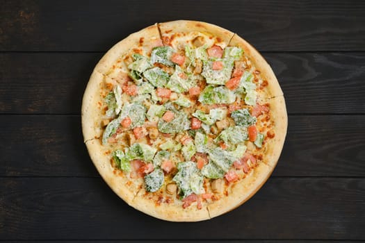 Pizza with fried chicken meat, lettuce and tomato on dark wooden table