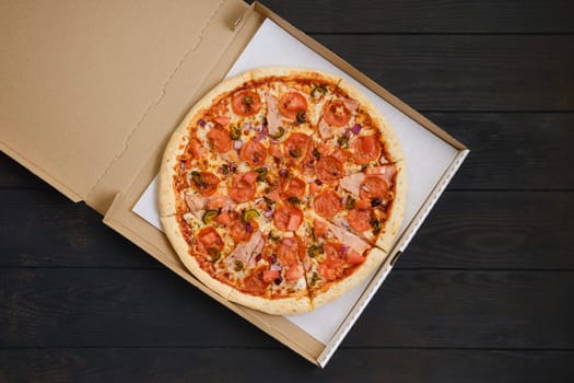 Pizza with pepperoni, ham, bell pepper, olives and red onion in cardboard package