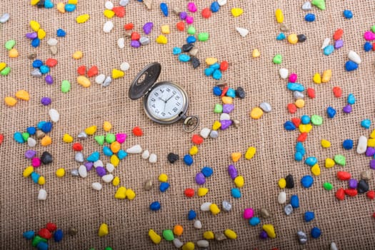 Pocket watch amid colorful pebbles on canvas background