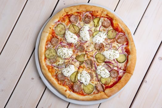 Top view of pizza with sausage, pickled cucumber, melted mozzarella and mushrooms