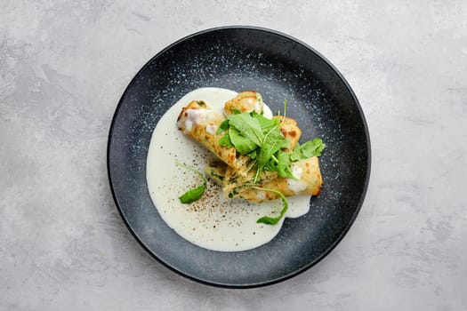 Top view of thin crepe stuffed with cheese, arugula and spinach on a plate with creamy sauce