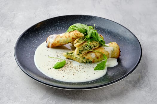 Thin crepe stuffed with cheese, arugula and spinach on a plate with creamy sauce