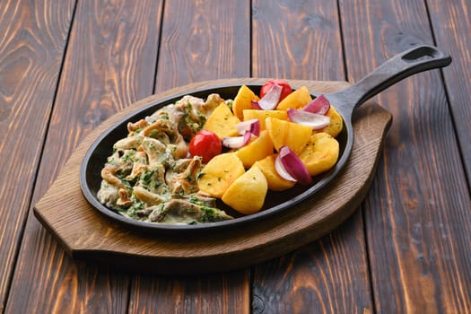 Cast iron skillet with fried chanterelles, honey mushrooms and potato wedges with creamy sauce