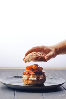 Making burger with beef, bacon, pumpkin and tomato - male hand puts bun on the top