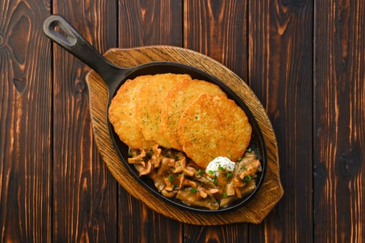 Cast iron skillet with fried chanterelles, honey mushrooms and potato pancakes with creamy sauce