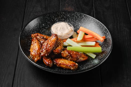 Roasted chicken wings, celery and carrot sticks and sauce on a plate
