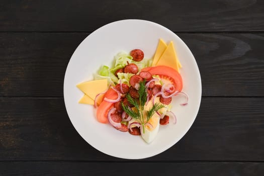 Salad with fried sausage, tomato, boiled egg, red onion and cheddar on dark wooden background