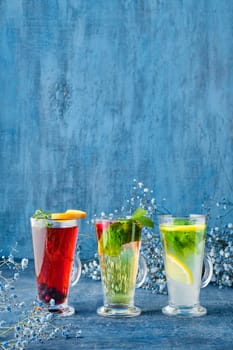 Three glasses with hot fruit and herbal tea on blue background