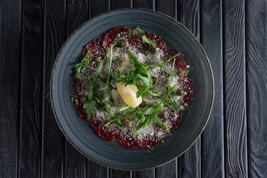 Top view of beef carpaccio with grated cheese, capers, lemon and ruccola