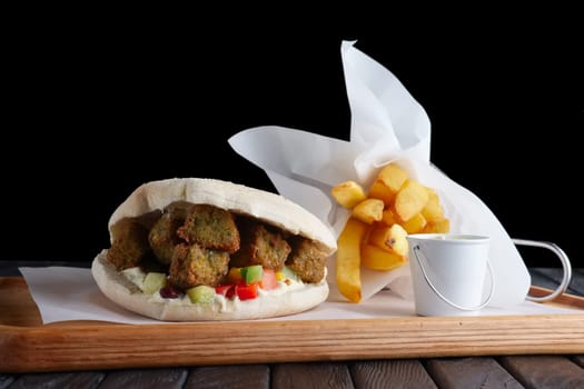 Pita bread with falafel, vegetables and fried potatos on wooden plate
