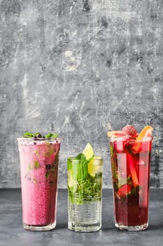 Three glasses with fruit refreshing drink on gray shabby background