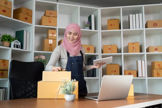 A Muslim entrepreneur prepares online orders, demonstrating her commitment to business success in a stylish office environment.