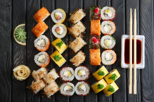 Big set of rolls, soy sauce and chopsticks (hashi) on dark background, top view