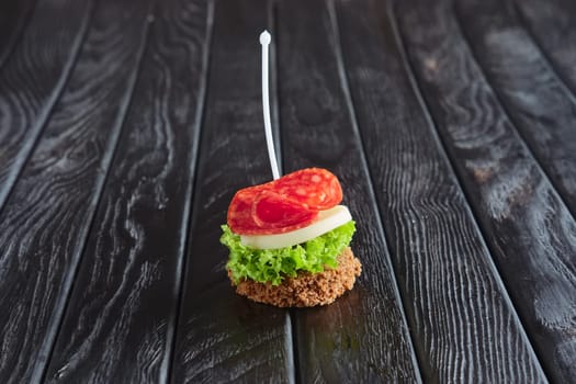 Appetizer for reception. Small sandwich with sausage, sheese and salad leaf on skewer