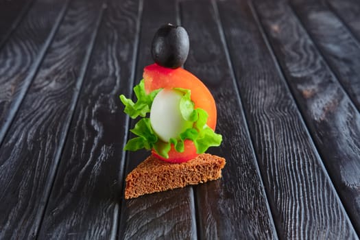Appetizer for reception. Brown bread with quail egg, tomato, salad leaf and olive on skewer