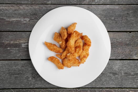 Crisp grilled chicken wings on a white dish on wooden table, top view.
