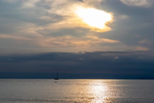 Evening sea pictures cloudy sky the sun is about to set I could see a sailboat holding sails in the distance. small in picture The sunlight reflects on the water surface.
