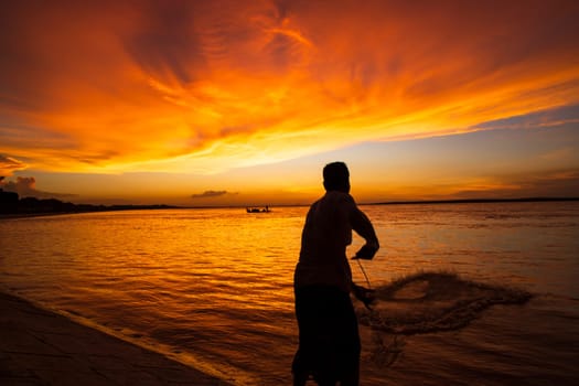 A Fisherman  Catching in fish On Sea Against orange Sky During Sunset