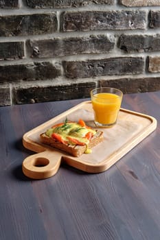 Sandwich with salmon, melted cheese and spicy sauce and a glass of orange juice