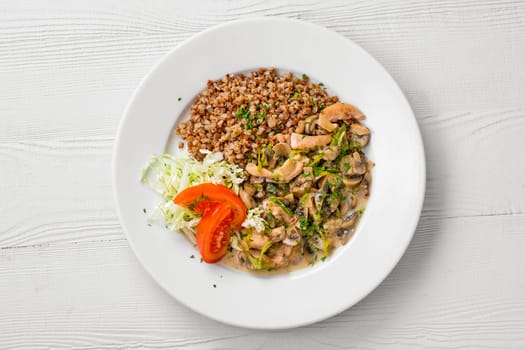 Top view of plate with chicken goulash, mushroom, buckwheat and tomato cabbage salad