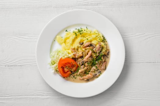 Top view of plate with chicken goulash, mushroom, mashed potato and tomato cabbage salad