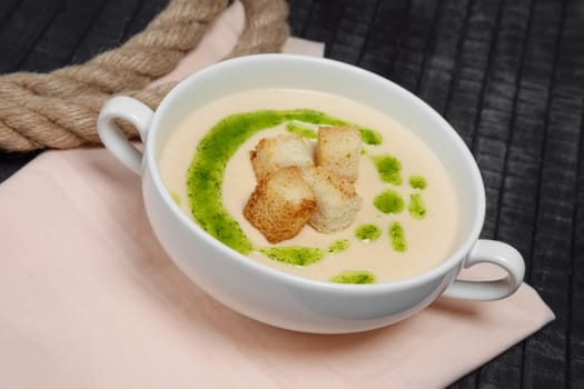 Creamy soup puree in white bowl and small pieces of fried bread toasts