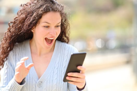 Excited woman checking amazing news on smart phone in the street