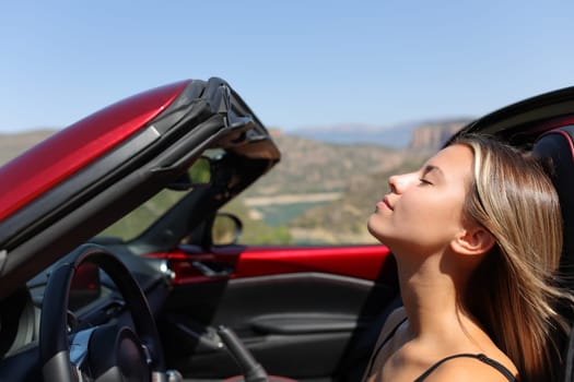 Relaxed driver breathing fresh air in a convertible car