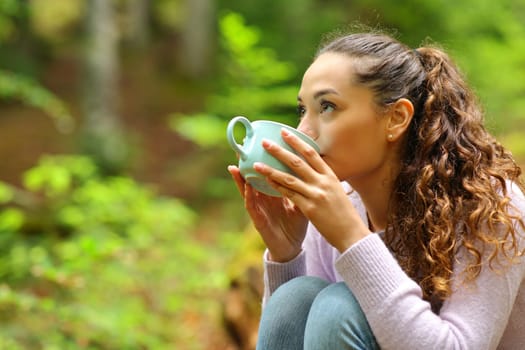 Woman drinking coffee looking above in a forest