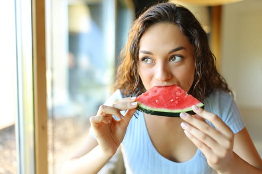 Woman in a restaurant eating watermelon looking through a window