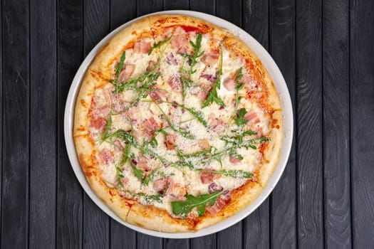 Top view of pizza with ham, bacon, arugula and grated parmesan cheese