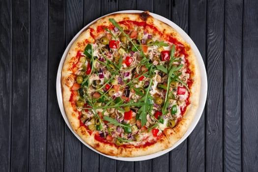 Top view of pizza with sausage, ham, olives, arugula, onion and tomato