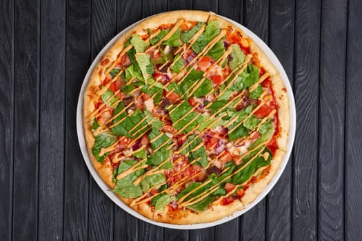 Top view of pizza with meat, pickled cucumber, onion, lettuce salad, tomato and barbecue sauce