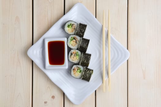 Top view of rolls with salmon, avocado and cucumber on plate with soy sauce and hashi