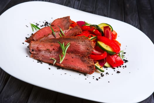 Roasted beef cutted on slices with grilled bell pepper, zucchini, onion and fresh rosemary