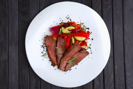 Top view of roasted beef cutted on slices with grilled bell pepper, zucchini, onion and fresh rosemary