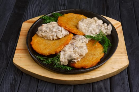 Potato flapjacks (draniki) with onion and mushroom creamy sauce in cast-iron pan