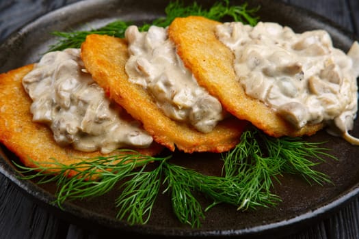 Closeup view of otato flapjacks (draniki) with onion and mushroom creamy sauce in cast-iron pan