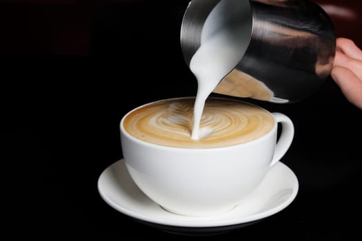 Pouring cream to cappuccino. Big white cup on black background.