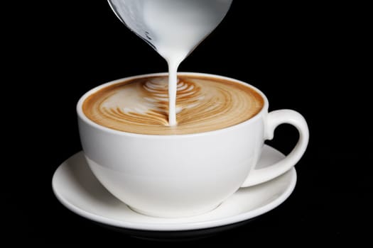 Pouring cream to cappuccino. Big white cup on black background.