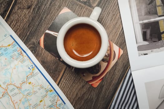 Cup of espresso near map and magazine on the table. Top point of view.